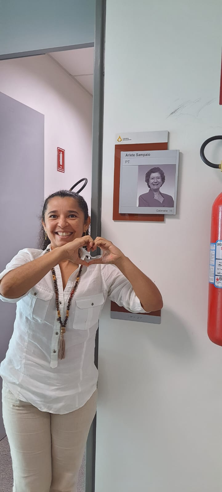 Bartiria Monteiro em frente à placa do gabinete da deputada Arlete Sampaio